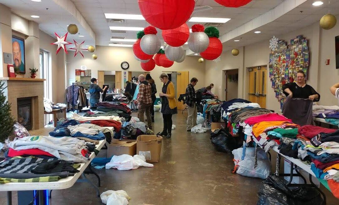 Photo shows multiple rows of clothing lining either side of a room, as members of the community look through them during a clothing swap in Knoxville, TN during 2019
